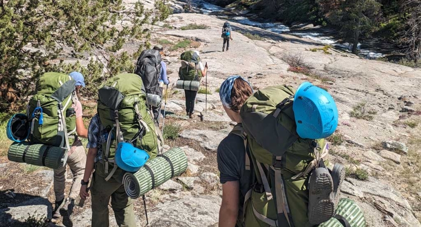 People wearing helmets and backpacks hike away from the camera up a rock incline. 